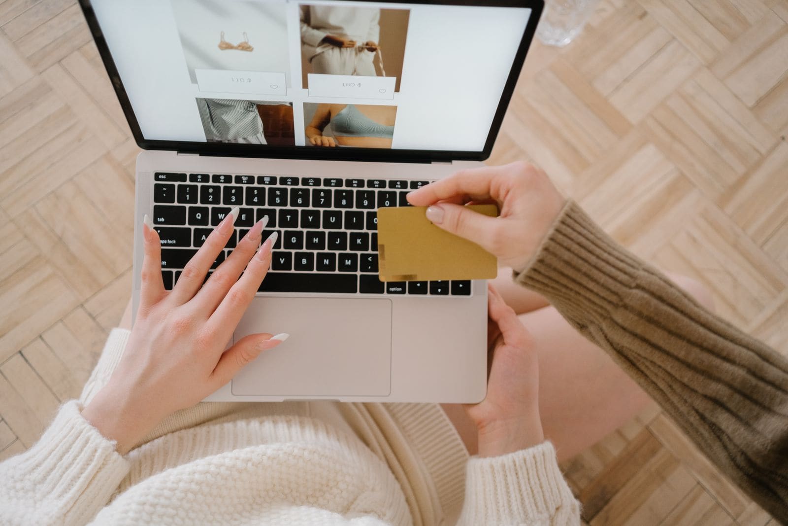 Pessoa pesquisando uma compra online em um notebook com cartão em mãos